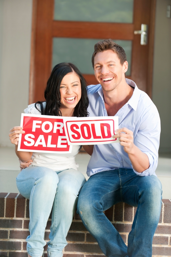 Happy couple holding for sale and sold signs in front of a new house